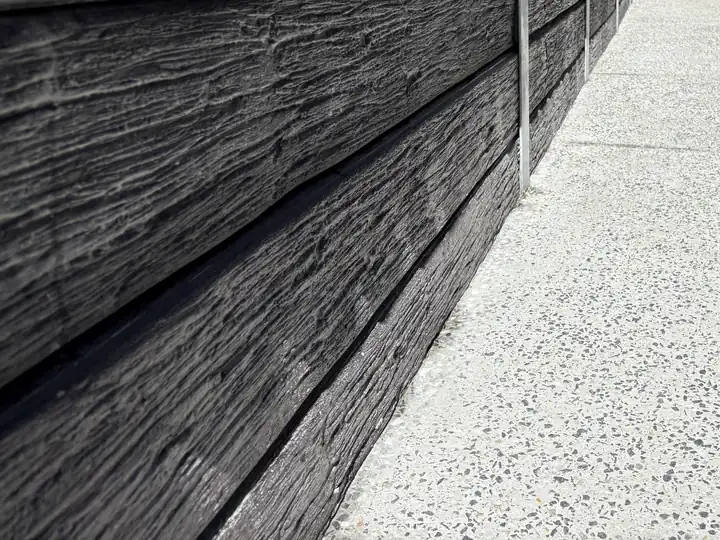 A light exposed aggregate house surround beside a charcoal timber-look concrete sleeper wall in Ripley