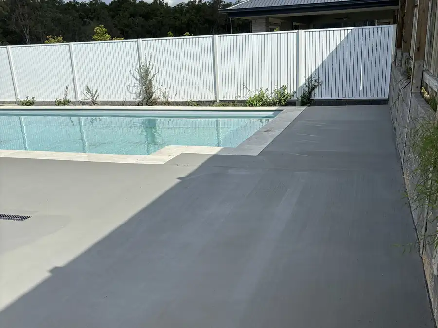 A smooth grey concrete pool surround running between a new pool and a white pool fence