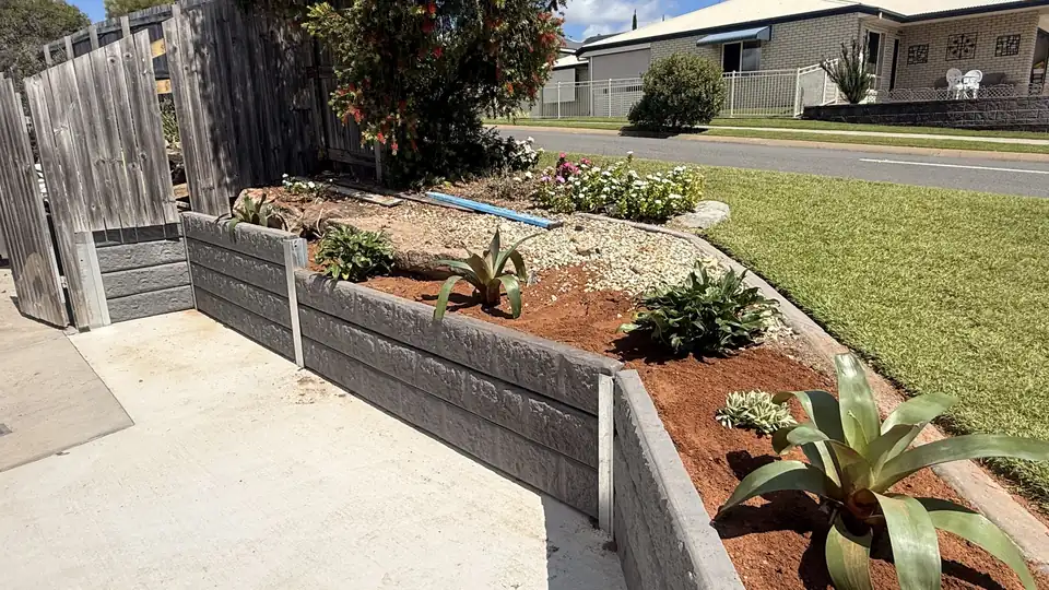 A charcoal concrete sleeper garden wall around a new garden bed with agave planting, beside a fresh concrete path